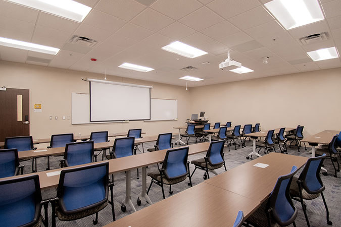 view of the classroom with lots or tables and seats with a smart screen at the front