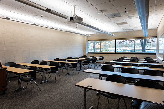 a room with tables and chairs with windows and a projector screen