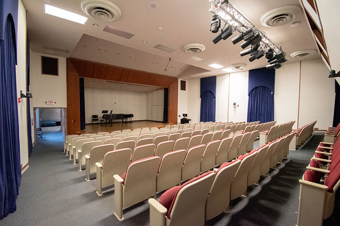 an auditorium featuring seating, lights and a stage that has a piano 