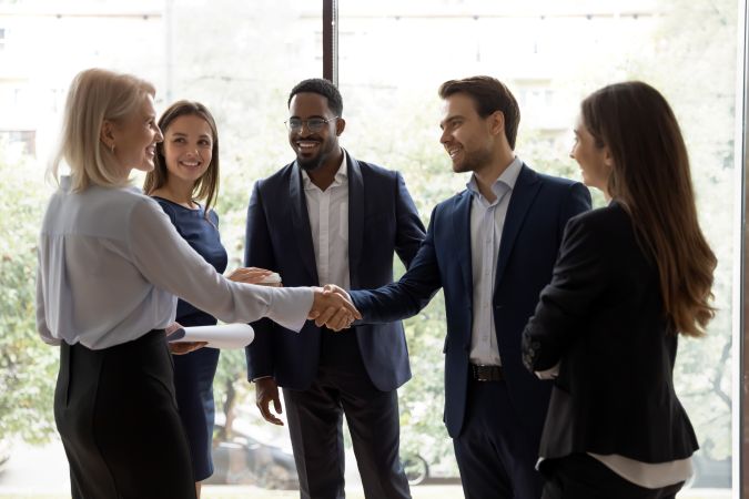5 business people standing in a hallway, two of them shaking hands