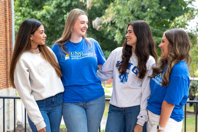 Four student workers laughing together, standing outside, wearing UNG Shirts