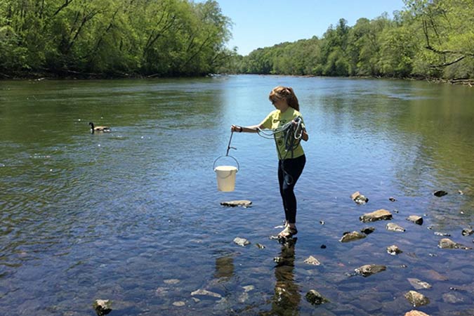 a woman grabbing a water sample from a creek for testing