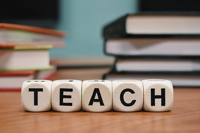 The word Teach on squares with books in background.