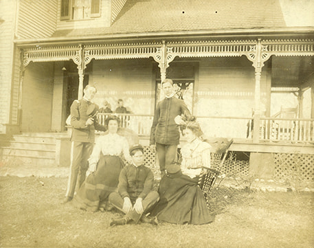 An aged photo of a family posing in front of a house.