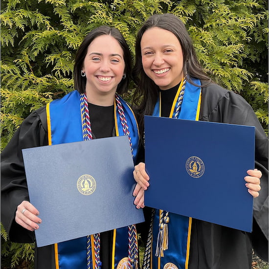 Two PSIA students in graduation attire display their new degrees.