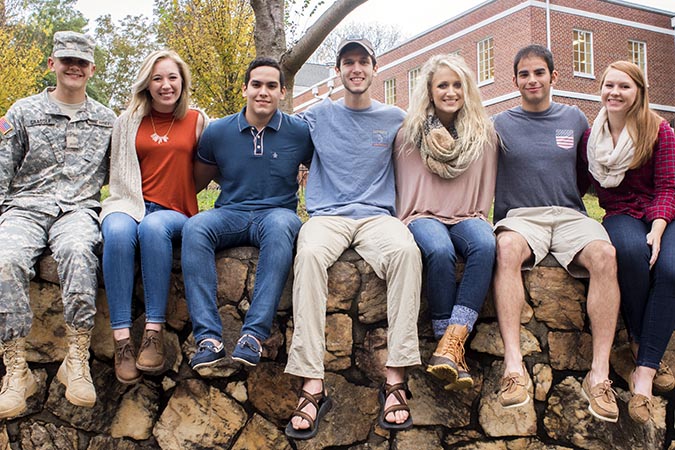 Students sitting on stone wall in the fall