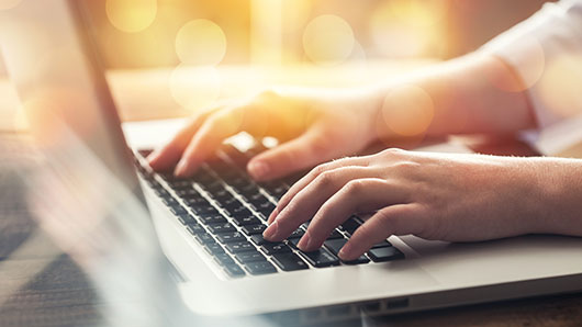 a person on a laptop using their keyboard with the suggestion they are filling out a registration form online